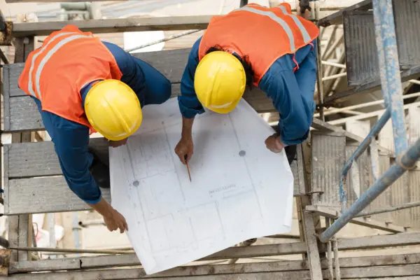 Zwei Bauleiter mit Helm besprechen einen Bauplan auf der Baustelle